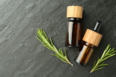 Essential oils in bottles and rosemary on gray textured table, flat lay. Space for text