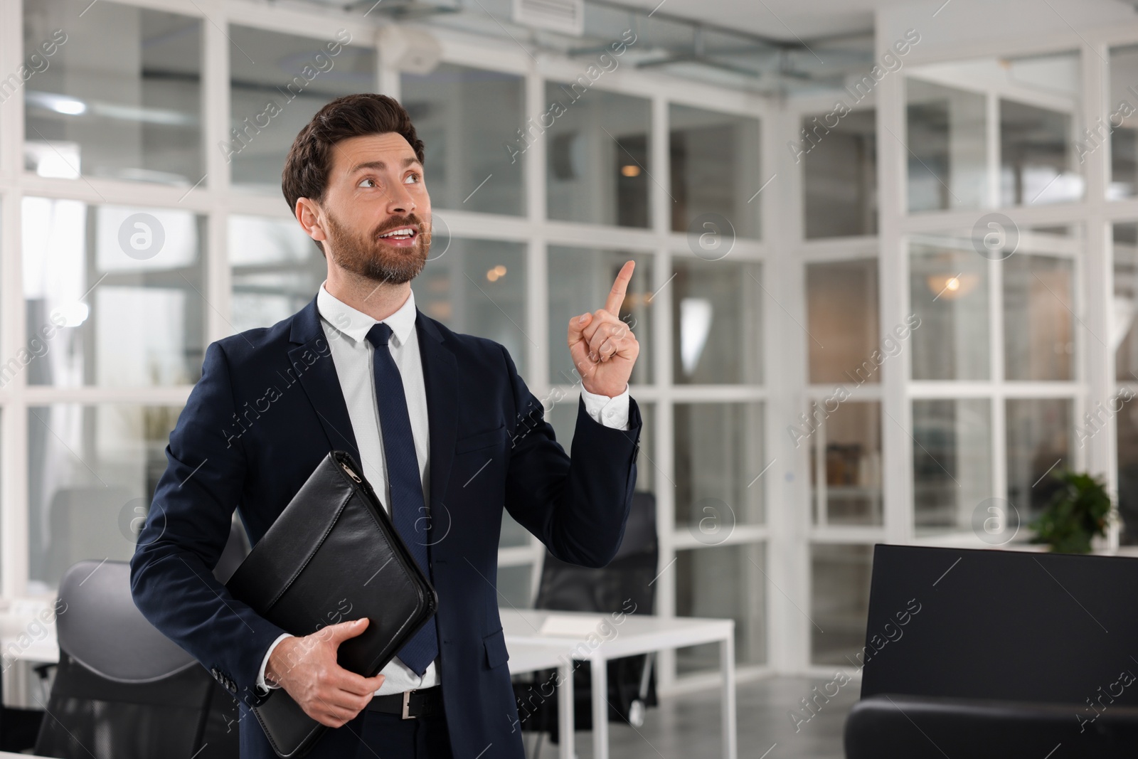 Photo of Real estate agent with leather portfolio pointing indoors. Space for text