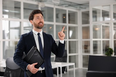 Real estate agent with leather portfolio pointing indoors. Space for text