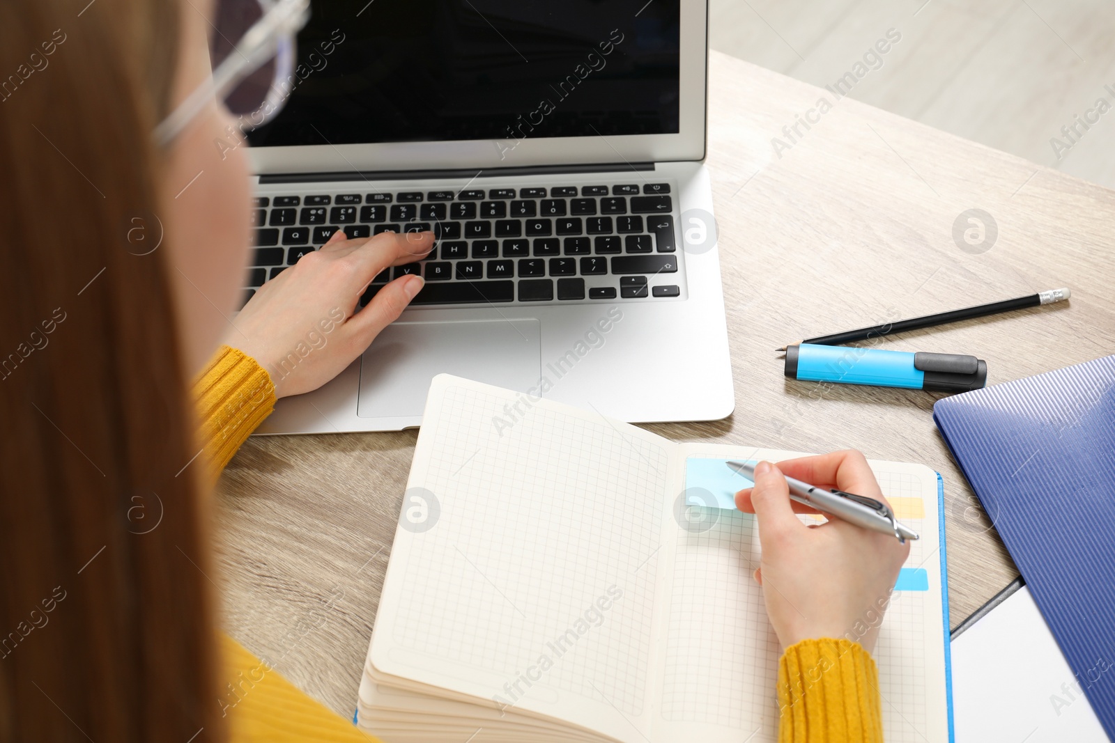 Photo of Woman taking notes while using laptop at wooden table, closeup