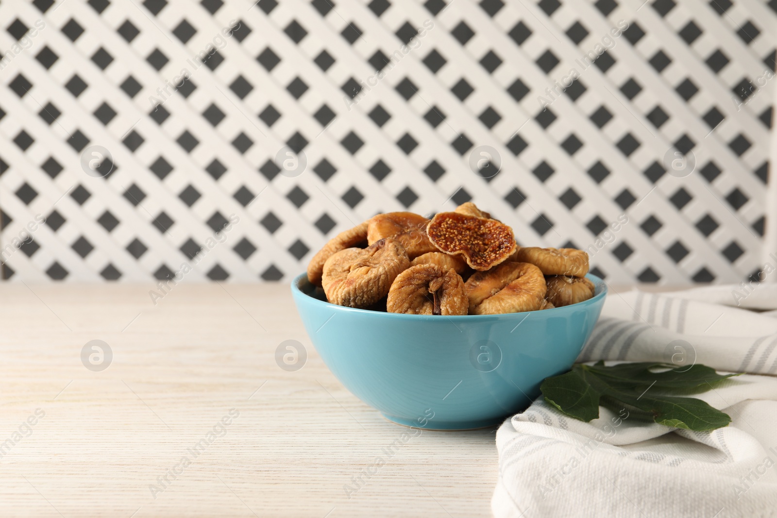 Photo of Bowl with tasty dried figs and green leaf on white wooden table. Space for text