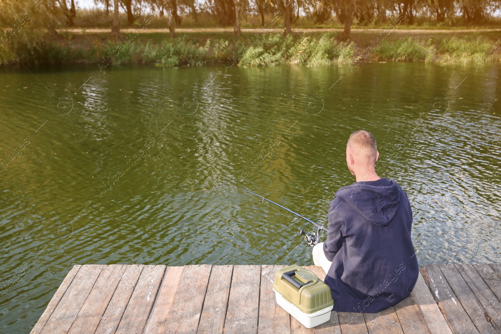 Photo of Man fishing on wooden pier at riverside. Recreational activity