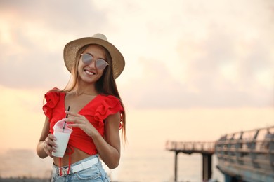 Beautiful young woman with tasty milk shake outdoors, space for text