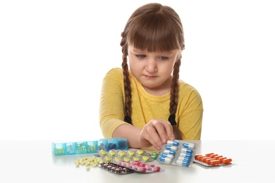 Photo of Crying little child with many different pills on white background. Danger of medicament intoxication