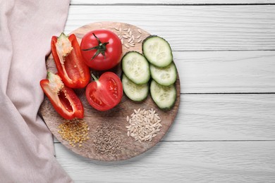 Photo of Fresh cucumbers, red bell peppers, tomatoes and vegetable seeds on white wooden table, top view. Space for text