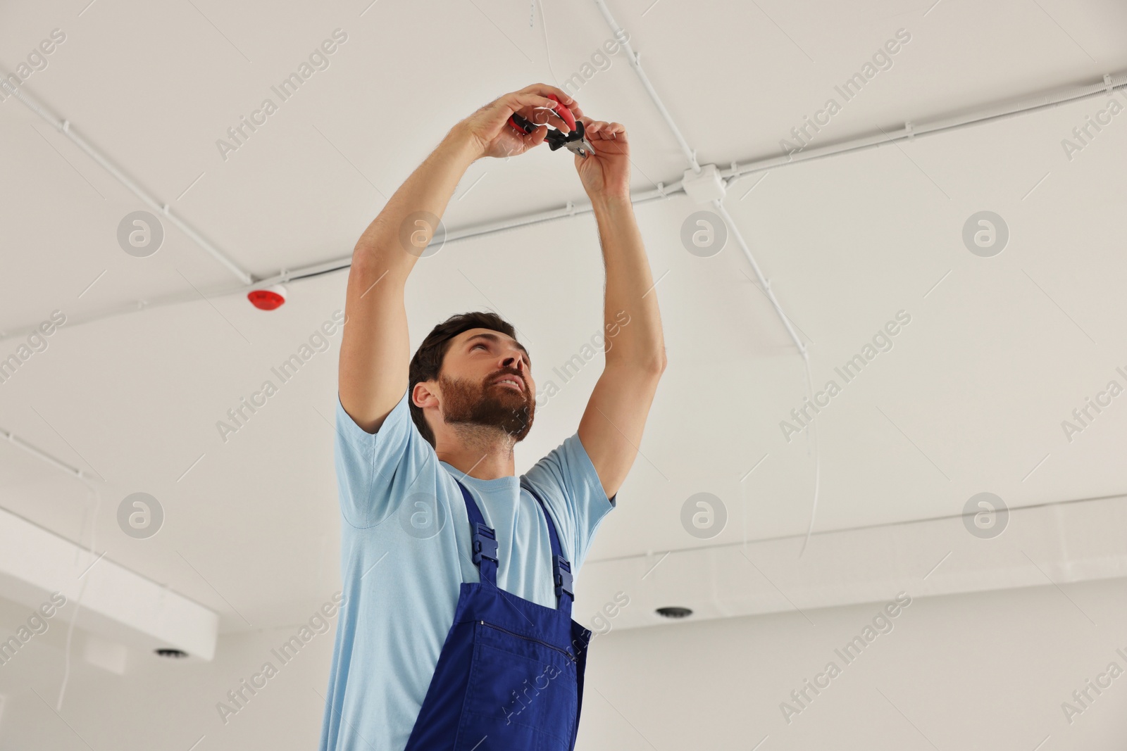 Photo of Electrician with pliers repairing ceiling wiring indoors