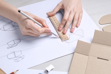 Woman creating packaging design at light wooden table, closeup