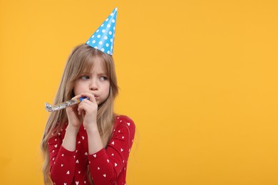 Photo of Bored little girl in party hat with blower on yellow background. Space for text
