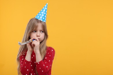 Bored little girl in party hat with blower on yellow background. Space for text