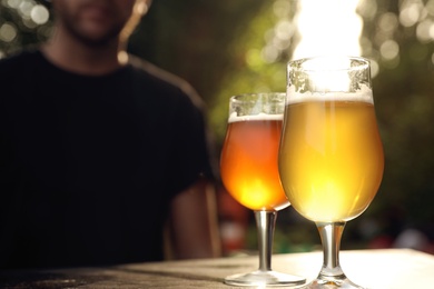 Glasses of cold tasty beer on wooden table outdoors