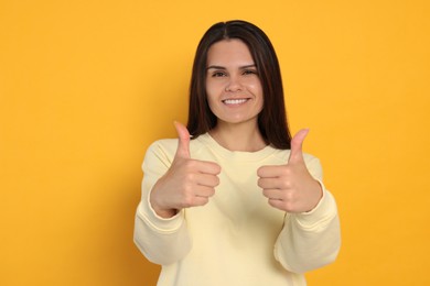Photo of Young woman showing thumbs up on orange background