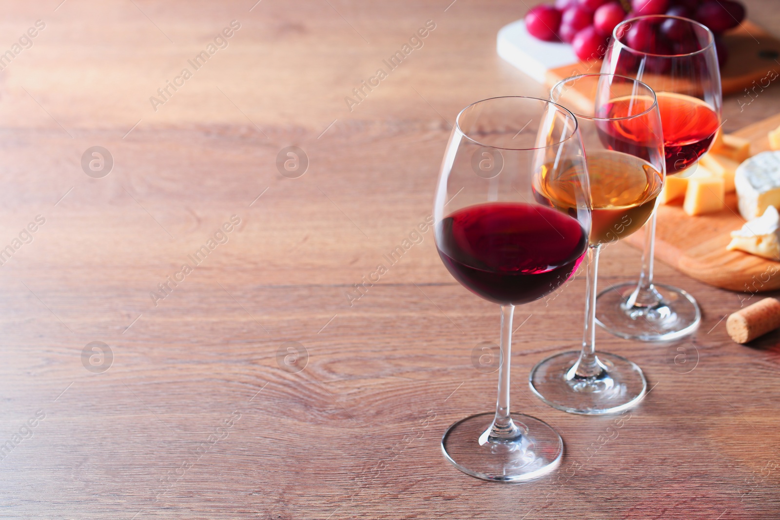 Photo of Glasses with different wines and appetizers on wooden table. Space for text