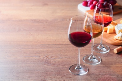 Photo of Glasses with different wines and appetizers on wooden table. Space for text