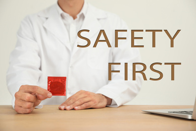 Safety first. Doctor holding condom at wooden table, closeup