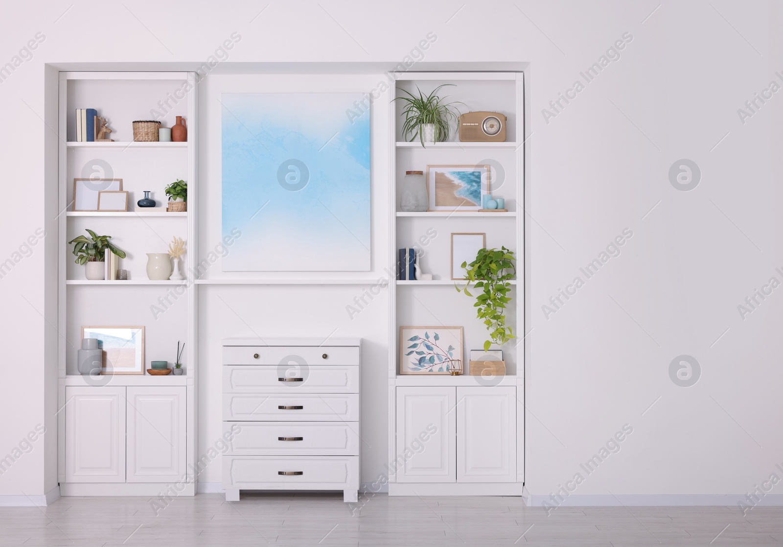 Photo of Interior design. Abstract picture and chest of drawers between shelves with accessories indoors, space for text