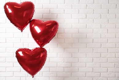 Photo of Red heart shaped balloons near white brick wall, space for text. Valentine's Day celebration
