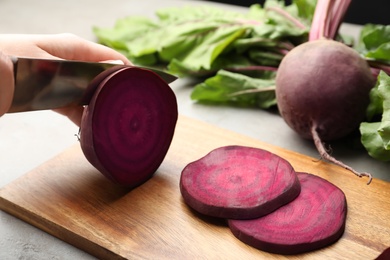 Photo of Woman cutting fresh red beet at table, closeup