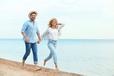 Happy romantic couple running together on beach, space for text