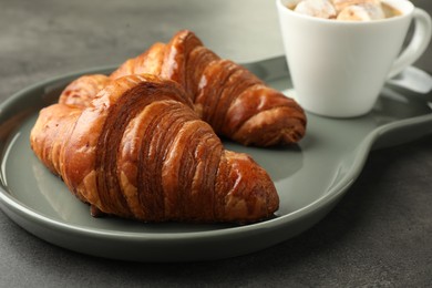 Tasty croissants served with cup of hot drink on grey textured table, closeup