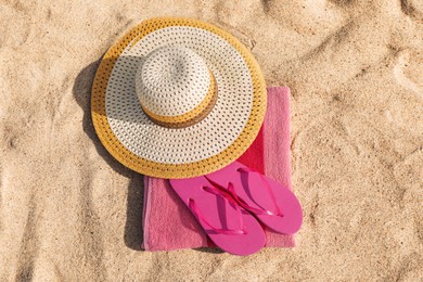 Beach towel with slippers and straw hat on sand, flat lay