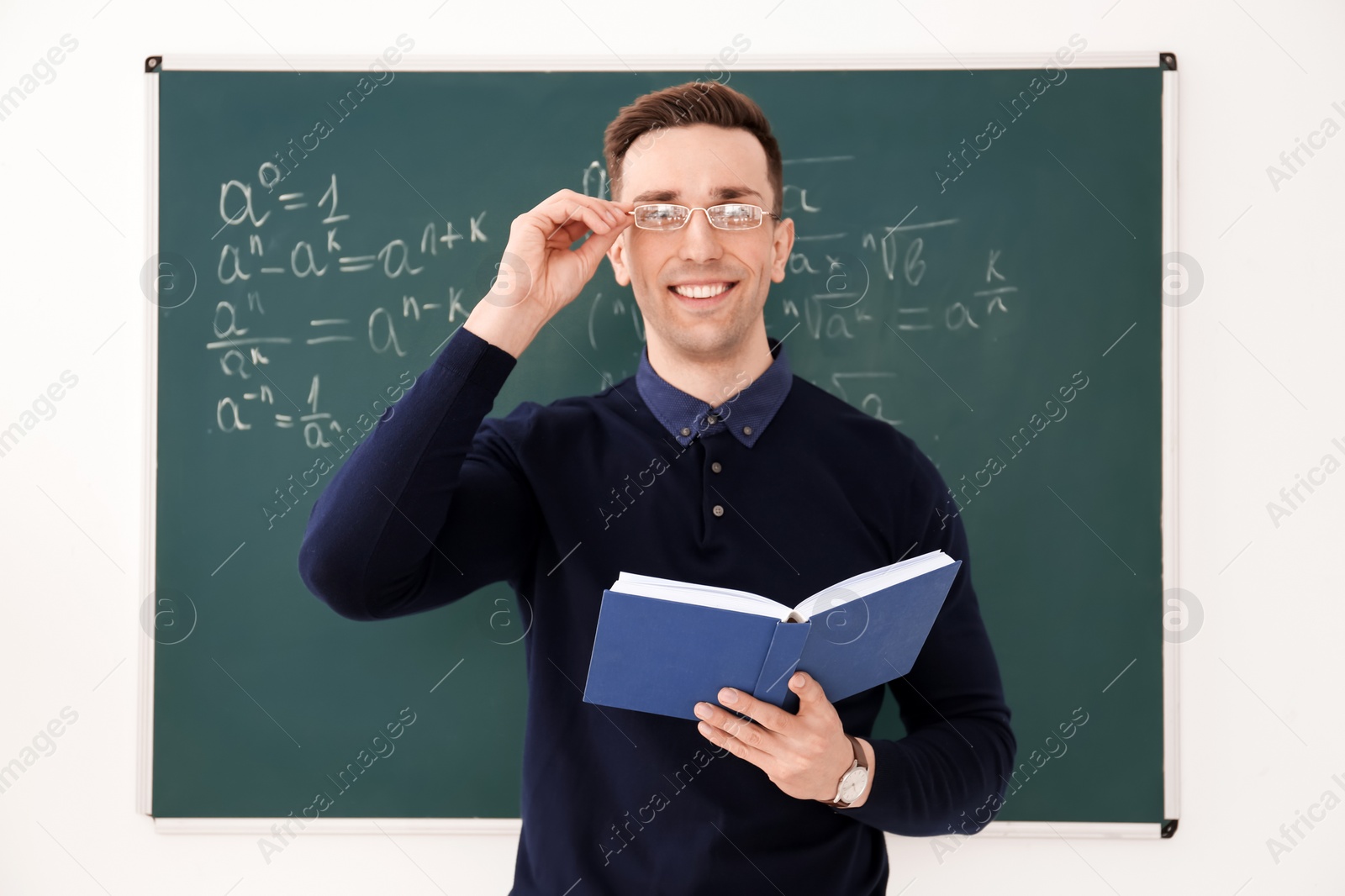 Photo of Young male teacher with book standing in classroom