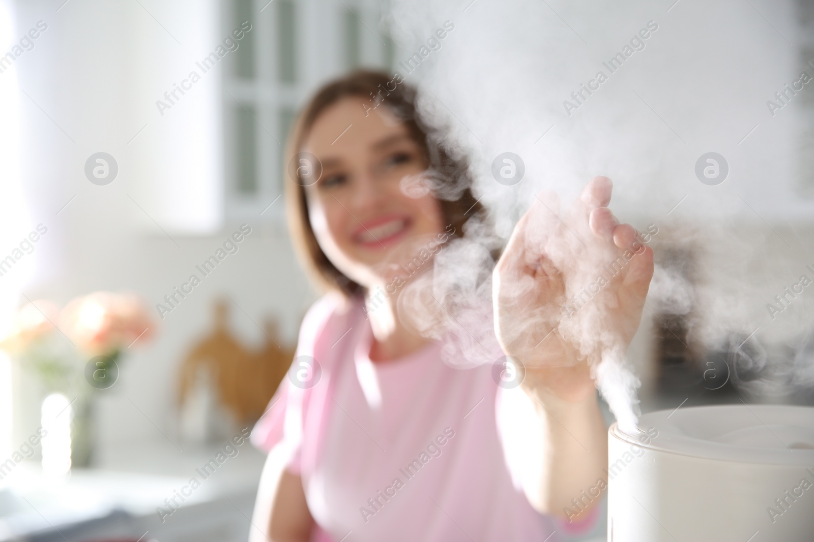 Photo of Woman near modern air humidifier in kitchen, focus on hand