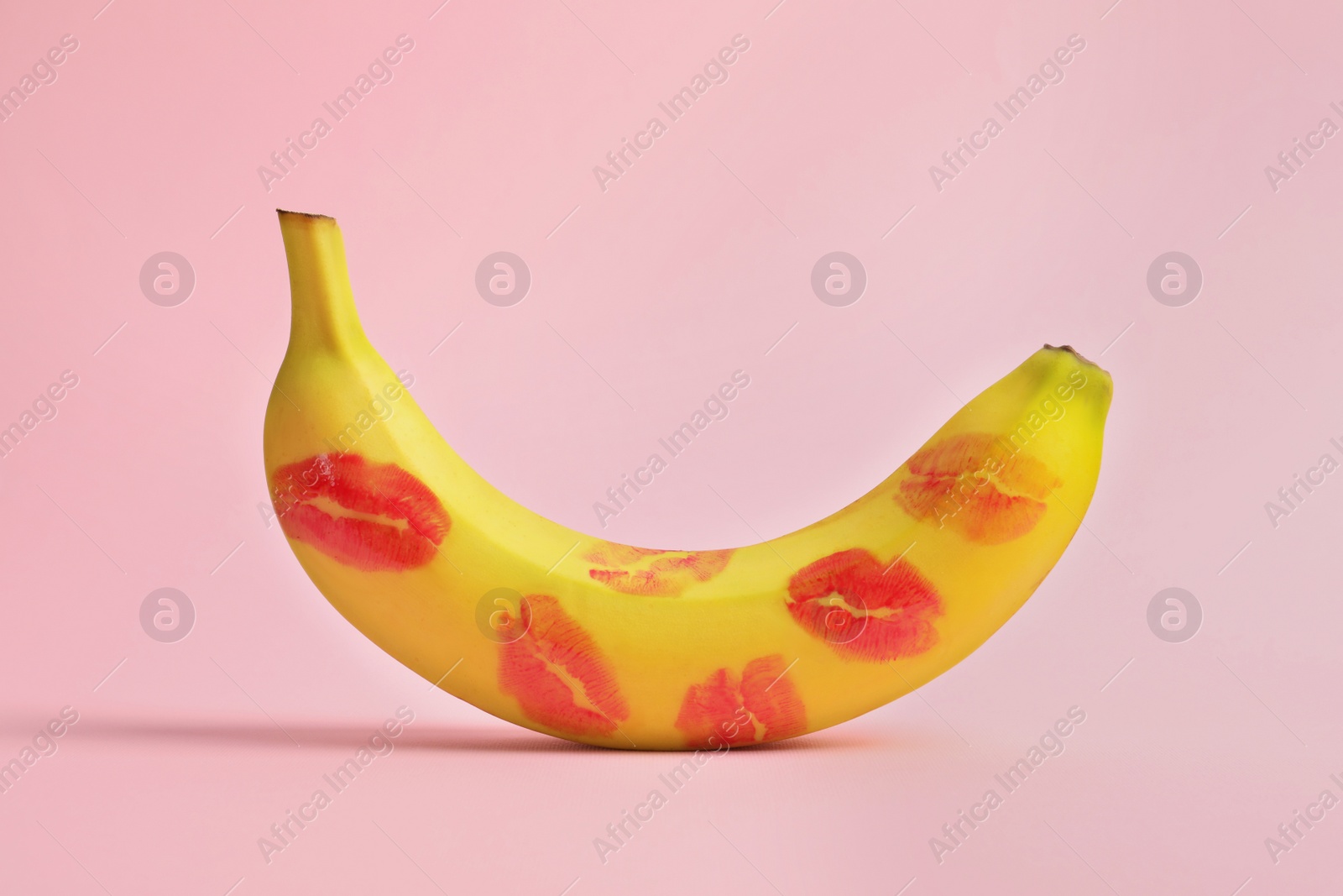 Photo of Banana covered with red lipstick marks on light pink background. Potency concept