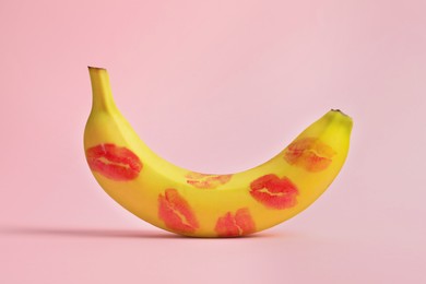 Photo of Banana covered with red lipstick marks on light pink background. Potency concept