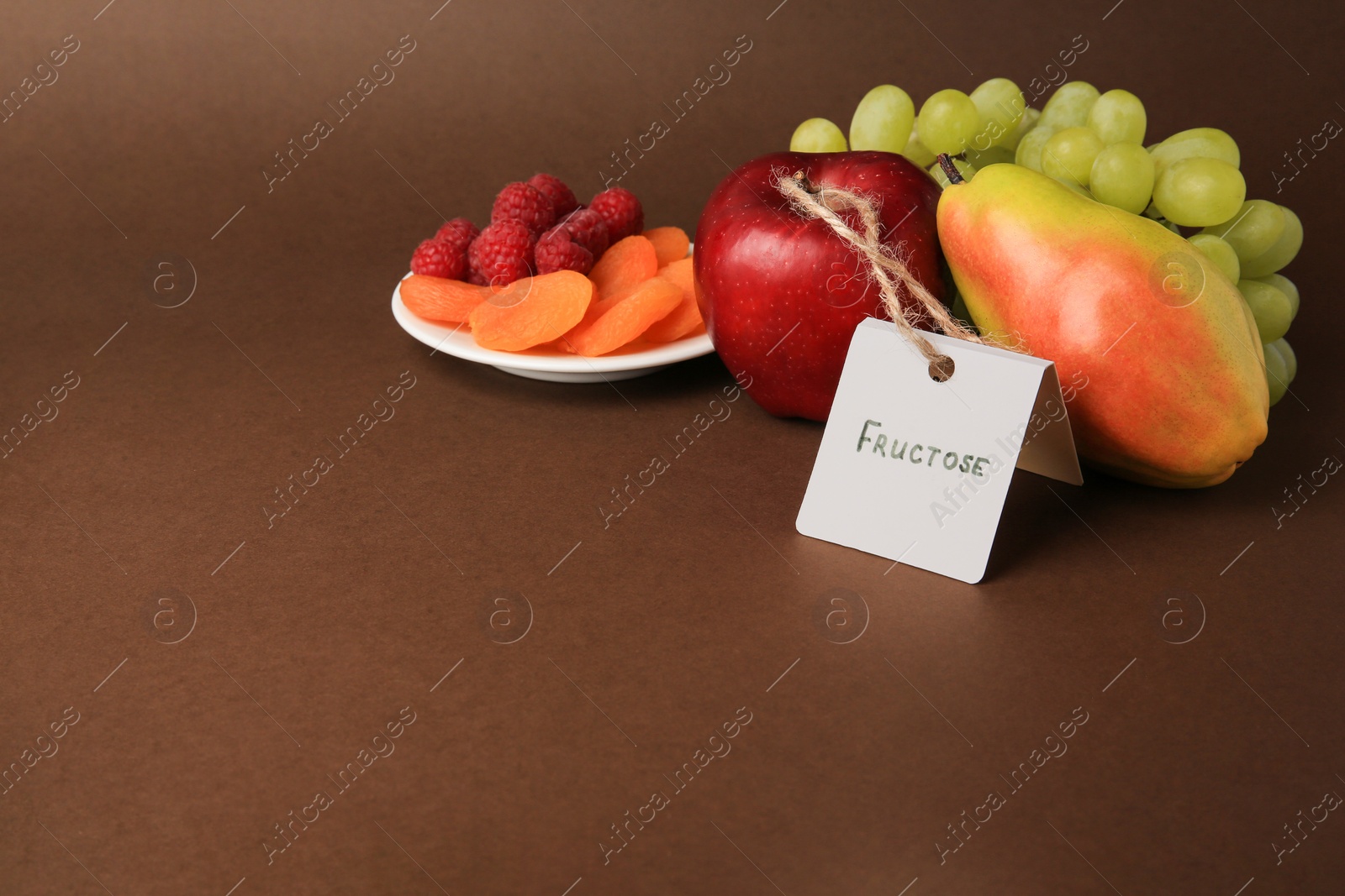 Photo of Card with word Fructose, delicious ripe fruits, raspberries and dried apricots on brown background. Space for text