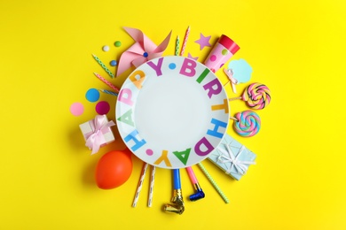 Different birthday party items and empty plate on yellow background, flat lay.  Space for text