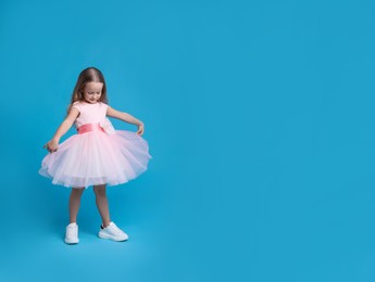 Photo of Cute little girl in beautiful dress dancing on light blue background. Space for text