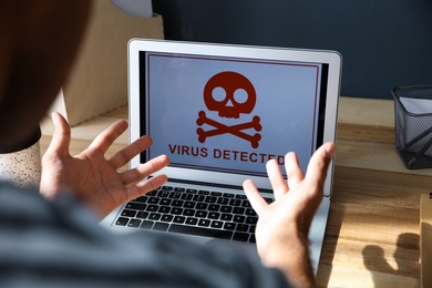 Photo of Man in front of laptop with warning about virus attack at workplace, closeup