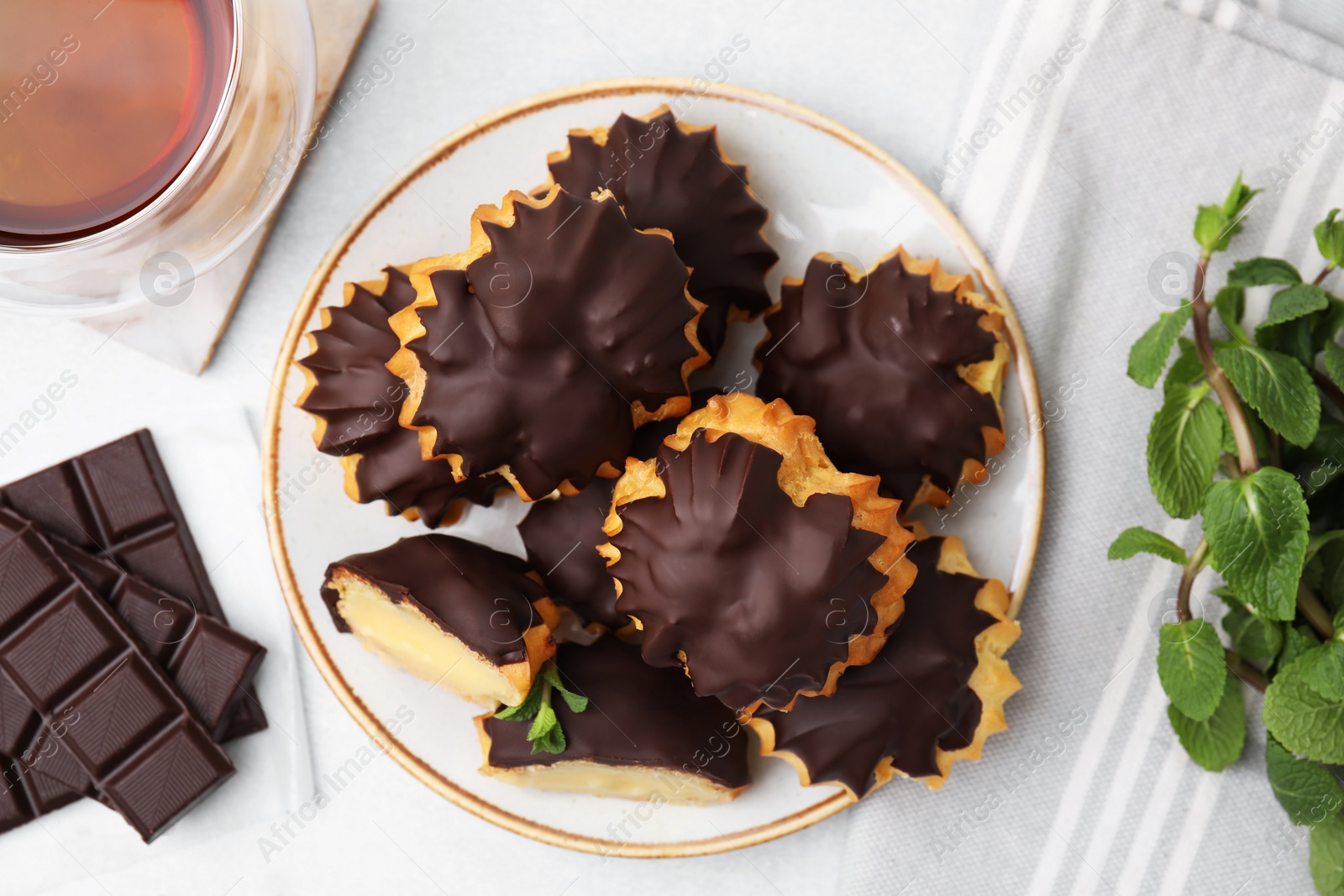 Photo of Delicious profiteroles with chocolate spread, cream and aromatic tea on white table, flat lay