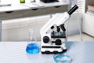 Photo of Laboratory analysis. Flask with blue liquid, petri dish and microscope on white table indoors