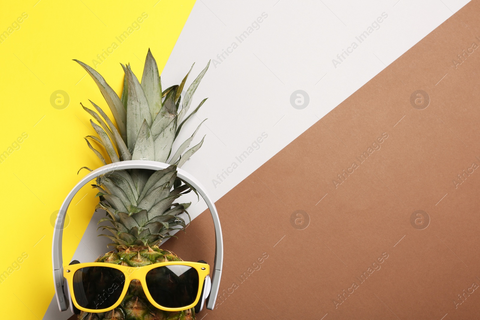Photo of Funny pineapple with headphones and sunglasses on color background, top view. Space for text
