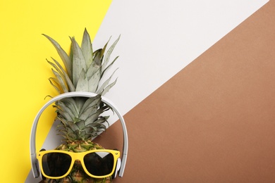 Photo of Funny pineapple with headphones and sunglasses on color background, top view. Space for text