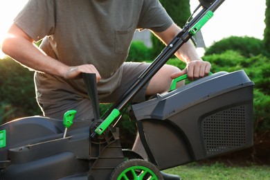Photo of Cleaning lawn mower. Man detaching grass catcher from device in garden, closeup