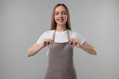 Photo of Beautiful young woman wearing kitchen apron on grey background. Mockup for design