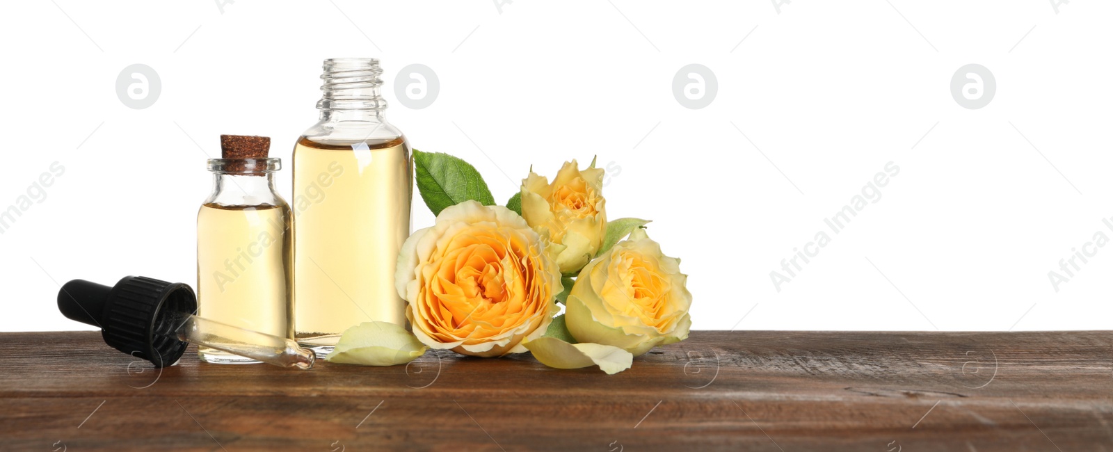 Photo of Bottles of rose essential oil and flowers on wooden table, white background