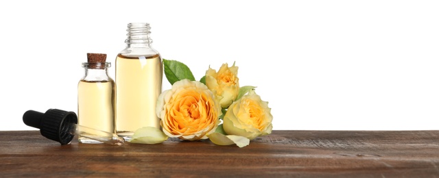 Photo of Bottles of rose essential oil and flowers on wooden table, white background