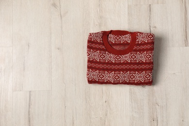 Photo of Warm folded Christmas sweater on light wooden table, top view. Space for text