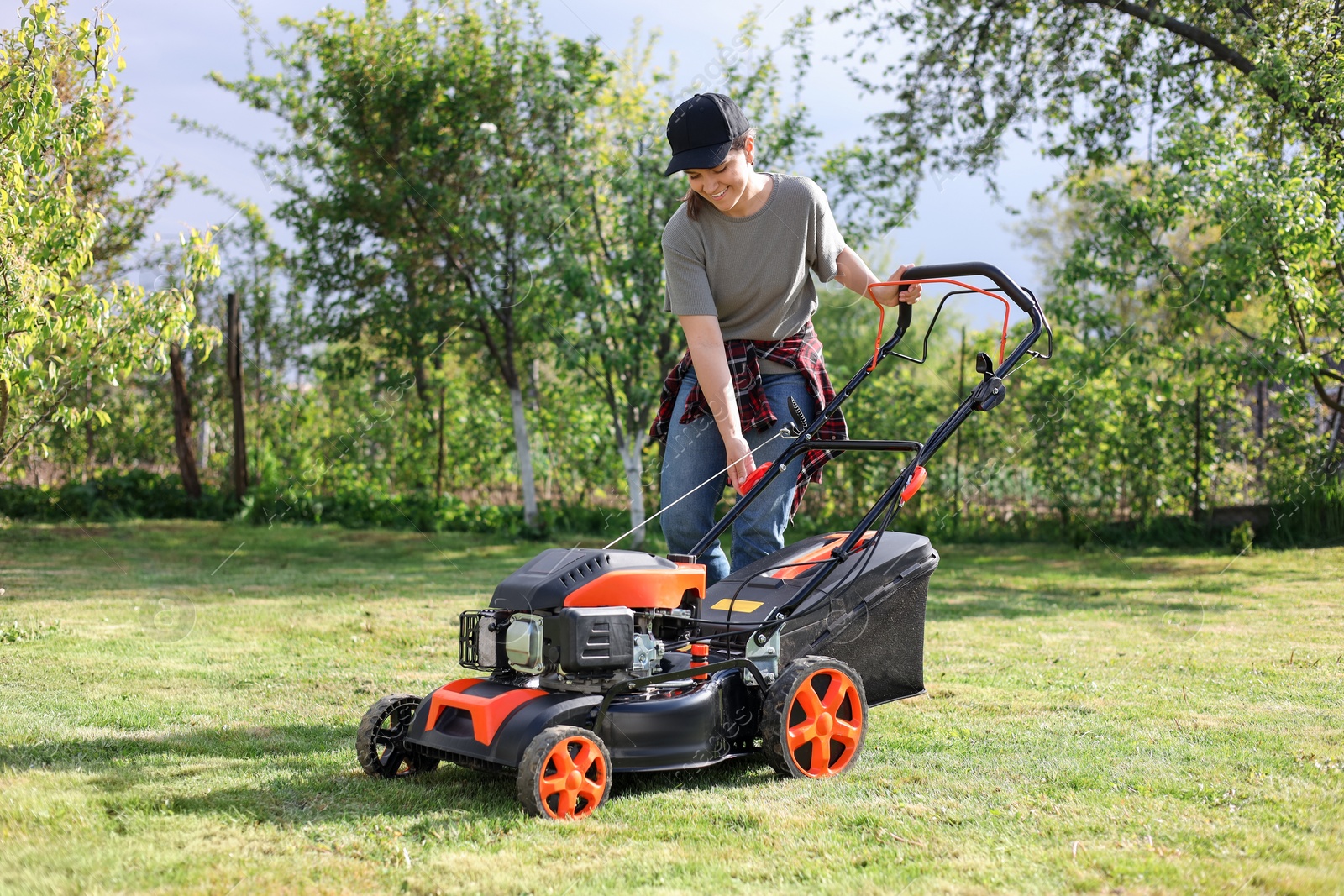 Photo of Smiling woman cutting green grass with lawn mower in garden