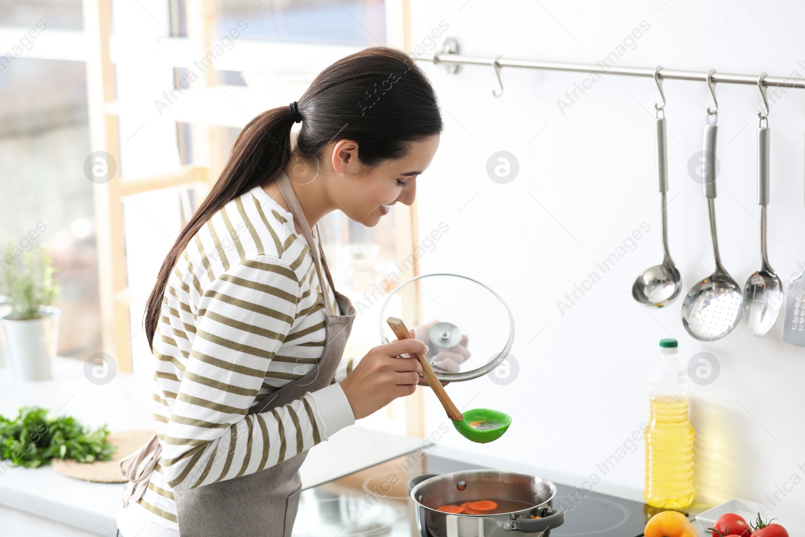 Photo of Young woman cooking tasty soup in kitchen