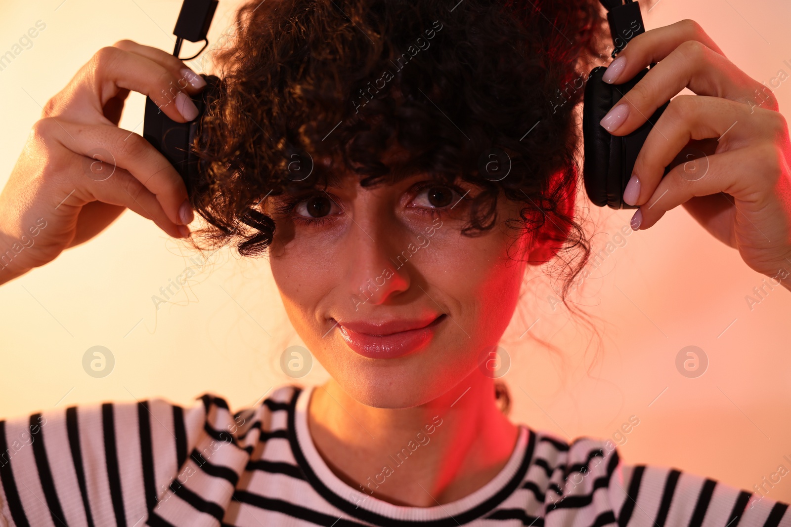 Photo of Beautiful young woman listening to music with headphones on color background in neon lights, closeup