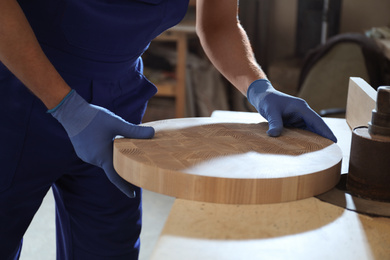 Photo of Professional carpenter grinding piece of wood in workshop, closeup