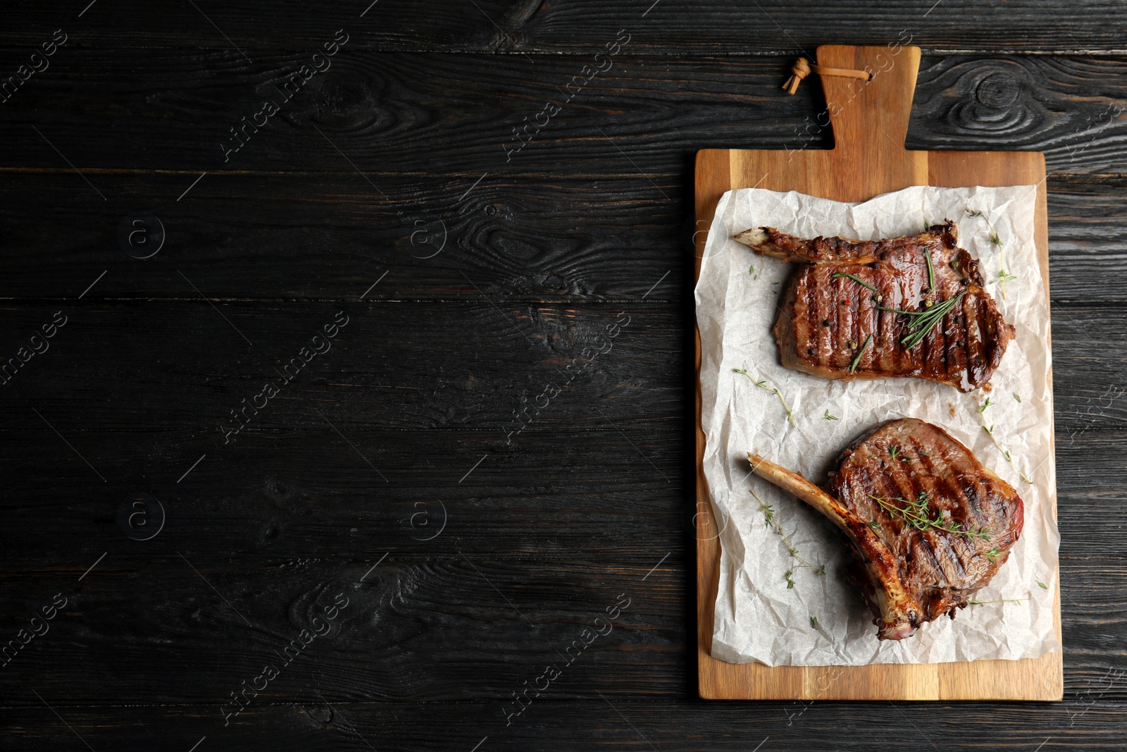 Photo of Board with grilled meat on wooden table, top view. Space for text