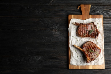 Photo of Board with grilled meat on wooden table, top view. Space for text