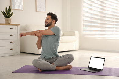Photo of Man practicing yoga while watching online class at home during coronavirus pandemic. Social distancing