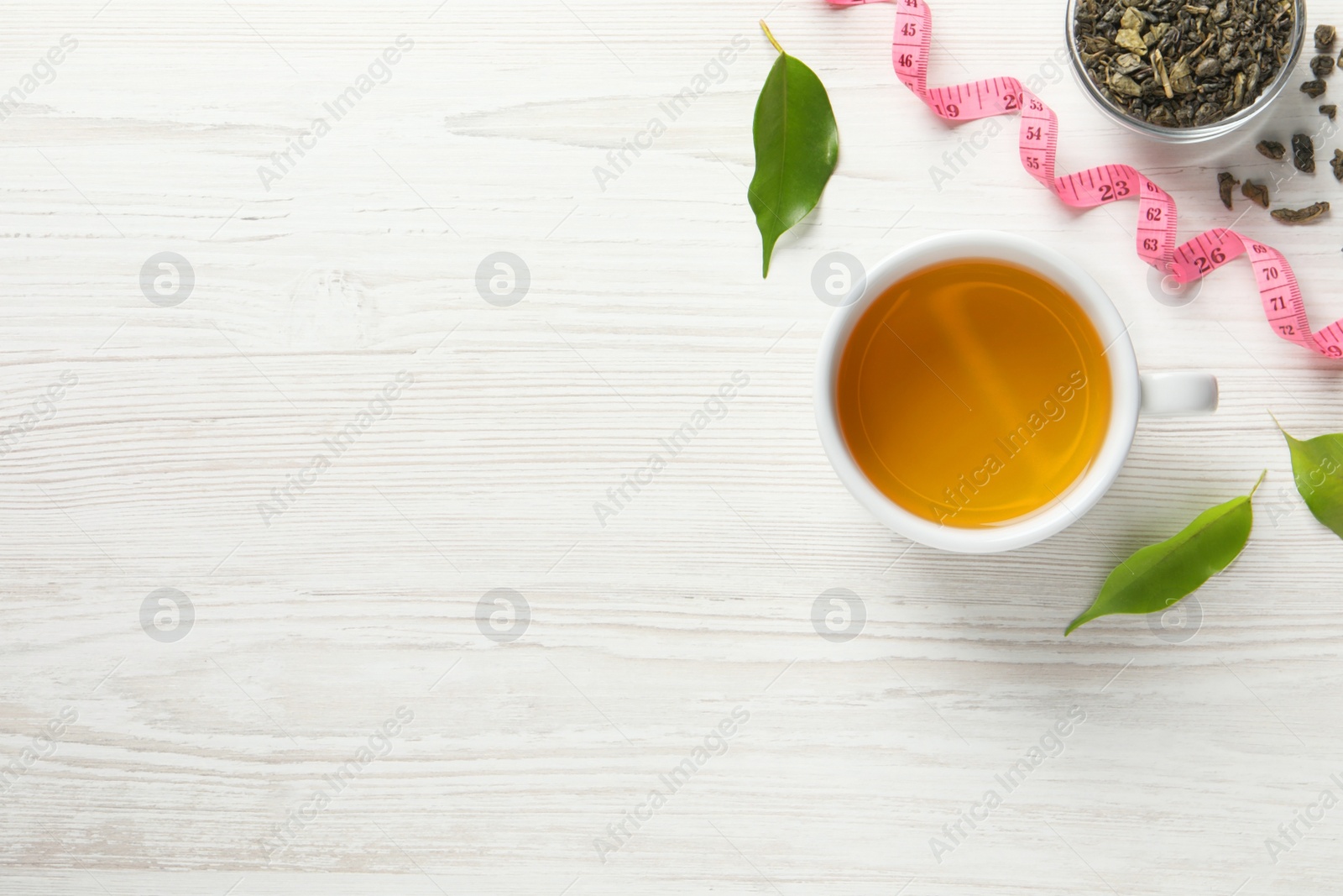 Photo of Flat lay composition with herbal diet tea and measuring tape on white wooden table, space for text. Weight loss concept