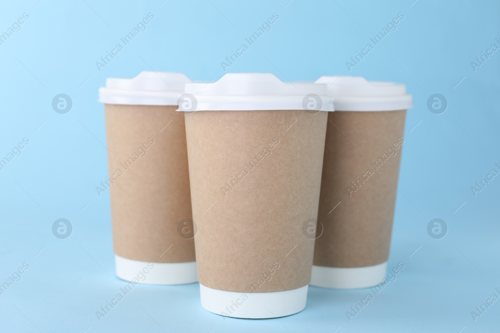 Photo of Paper cups with white lids on light blue background. Coffee to go